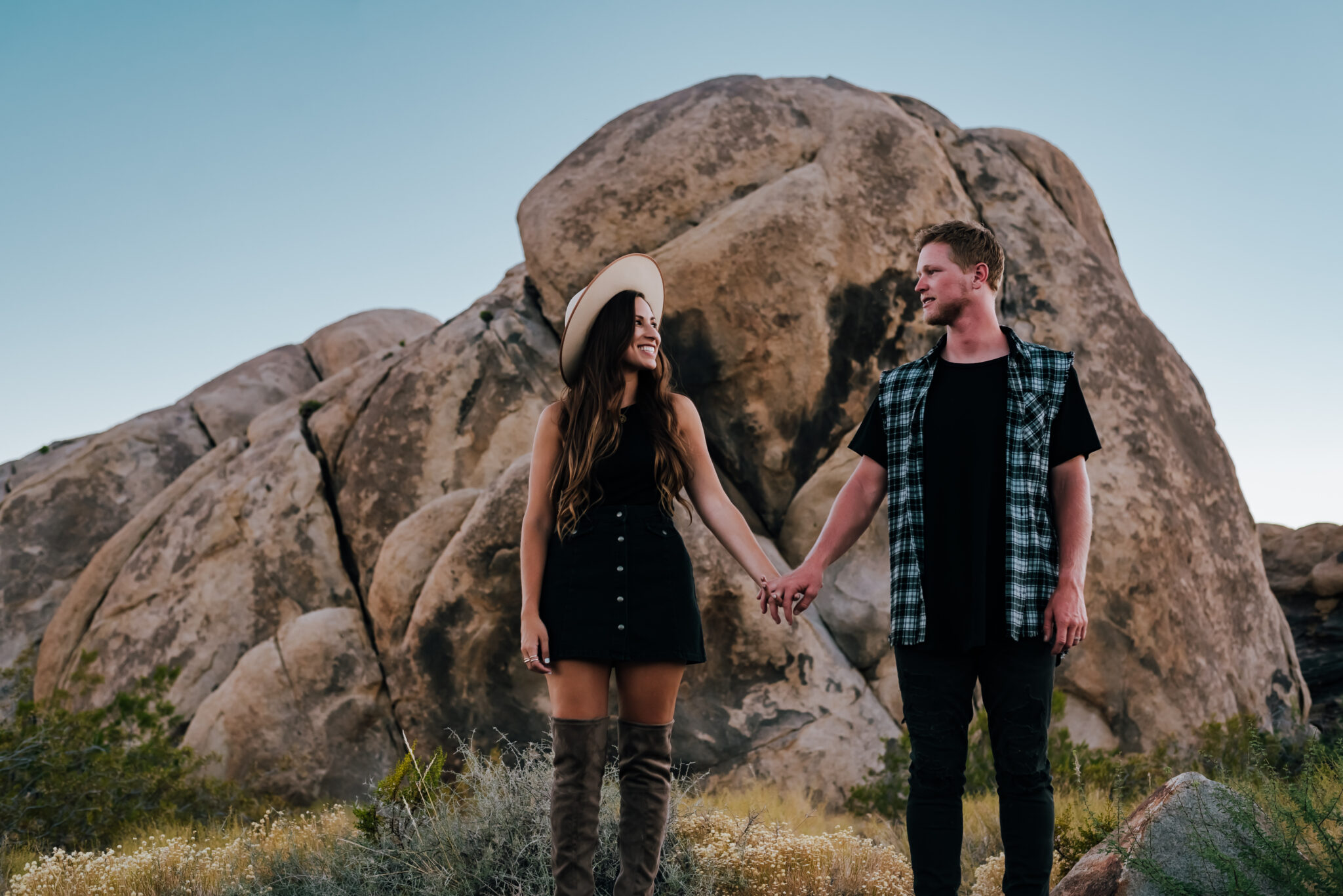 Couple holding hands and smiling  in front of giant boulder