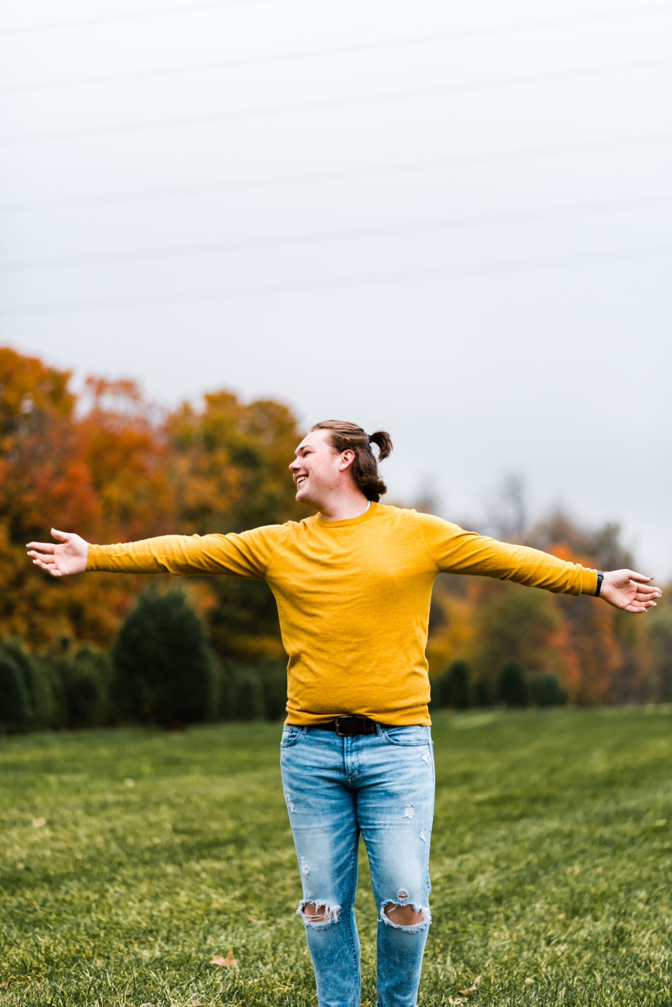 Boy in yellow sweater swings his arms around in a field of fall colors
