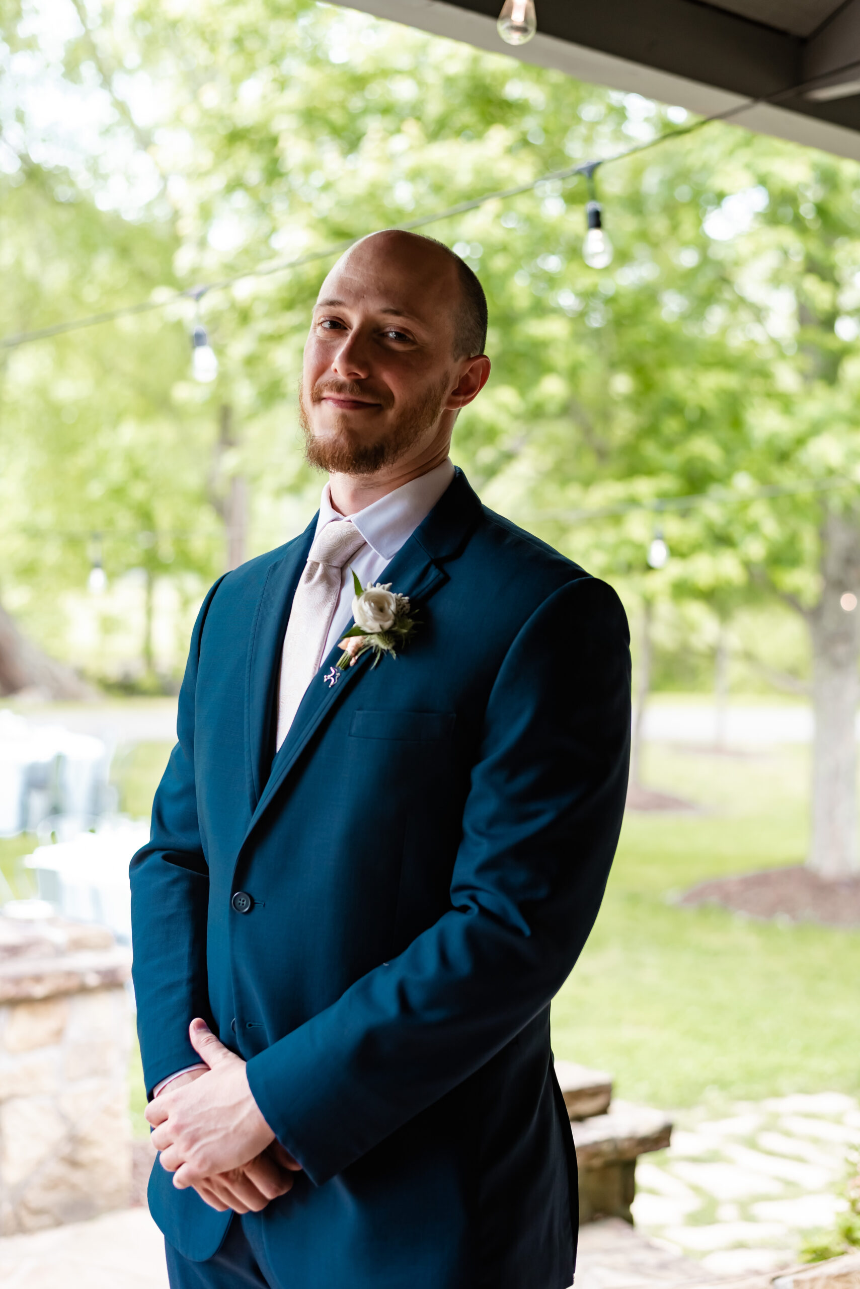 Groom stands in navy suit with hands clasped 