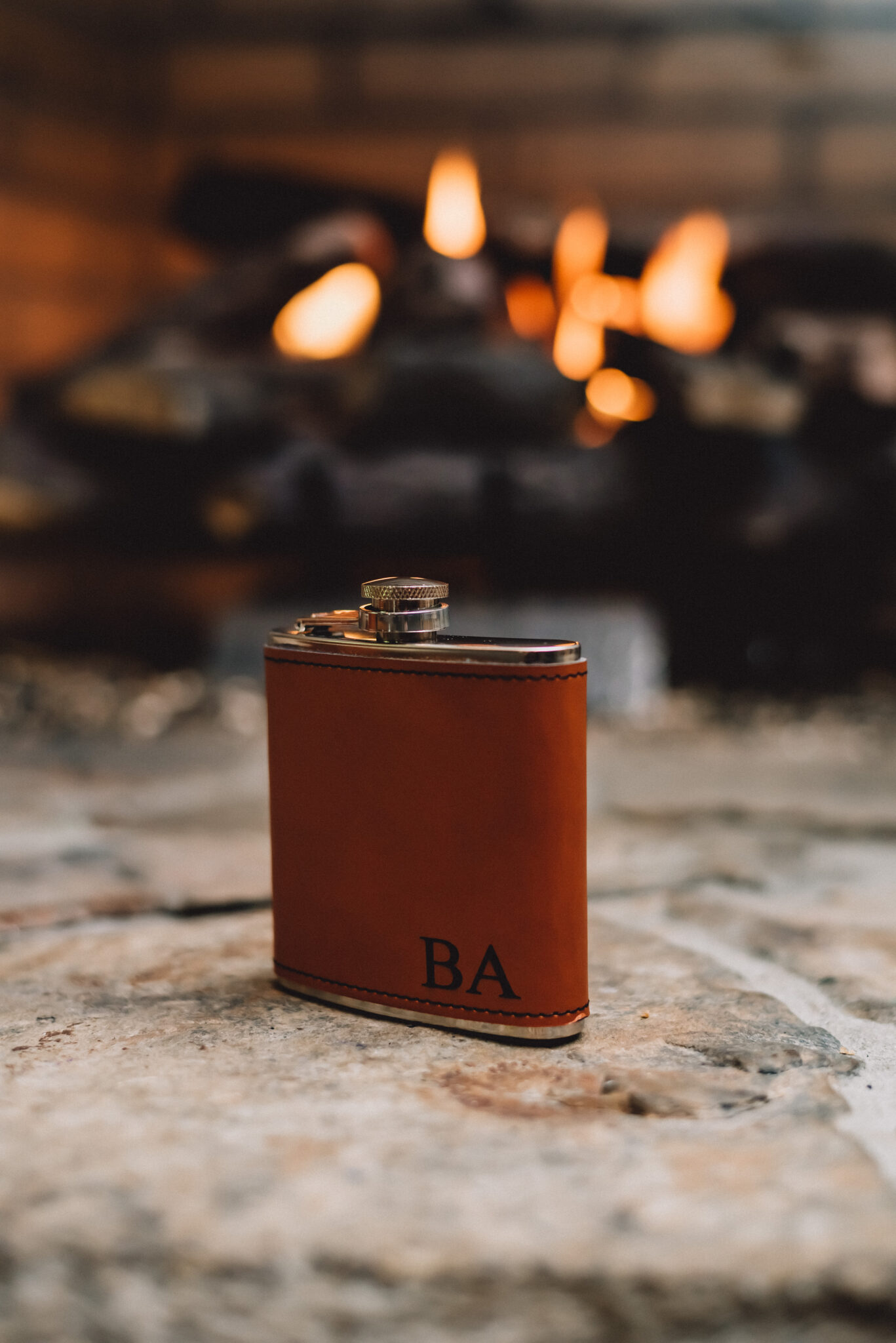 Groom's initials engraved into leather flask sits in front of fireplace