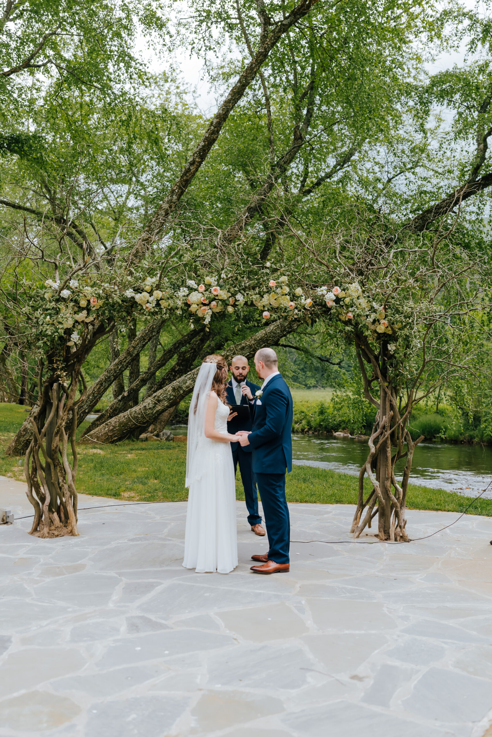 Bride, groom, and officiant stand in front of floral ceremony arch