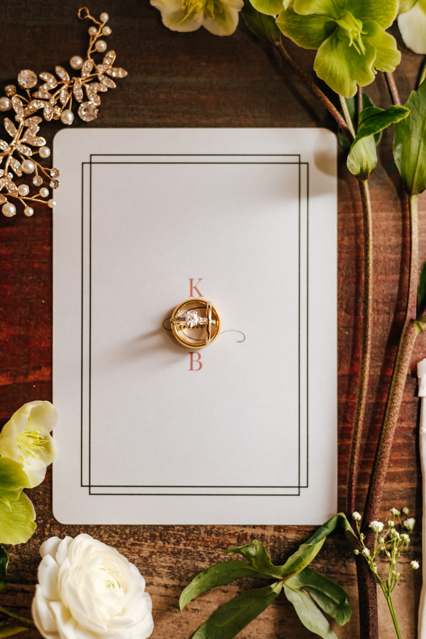 A simple white invitation with three gold rings arranged on top with greenery all around
