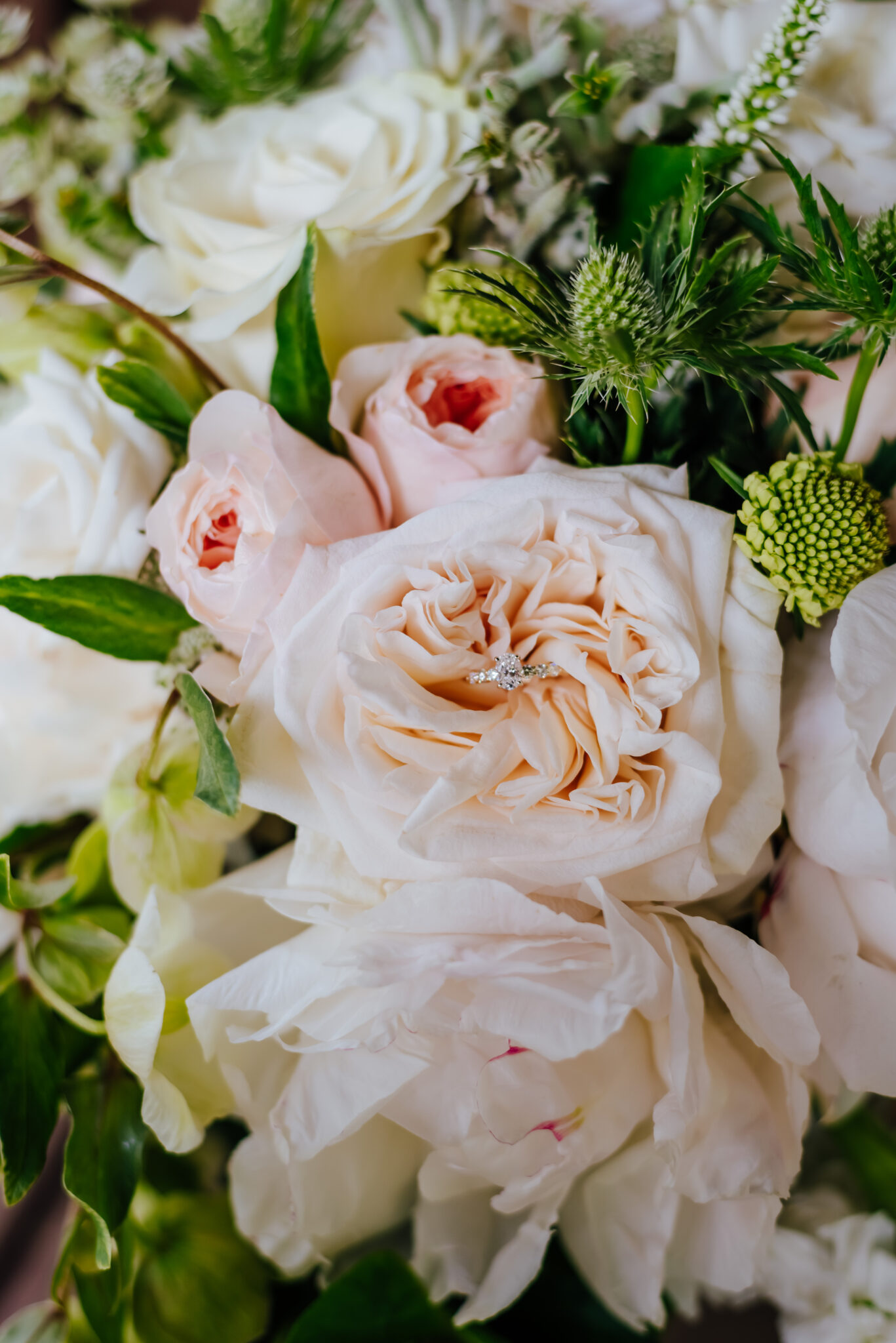 An engagement ring nestles in a blush pink peony bouquet