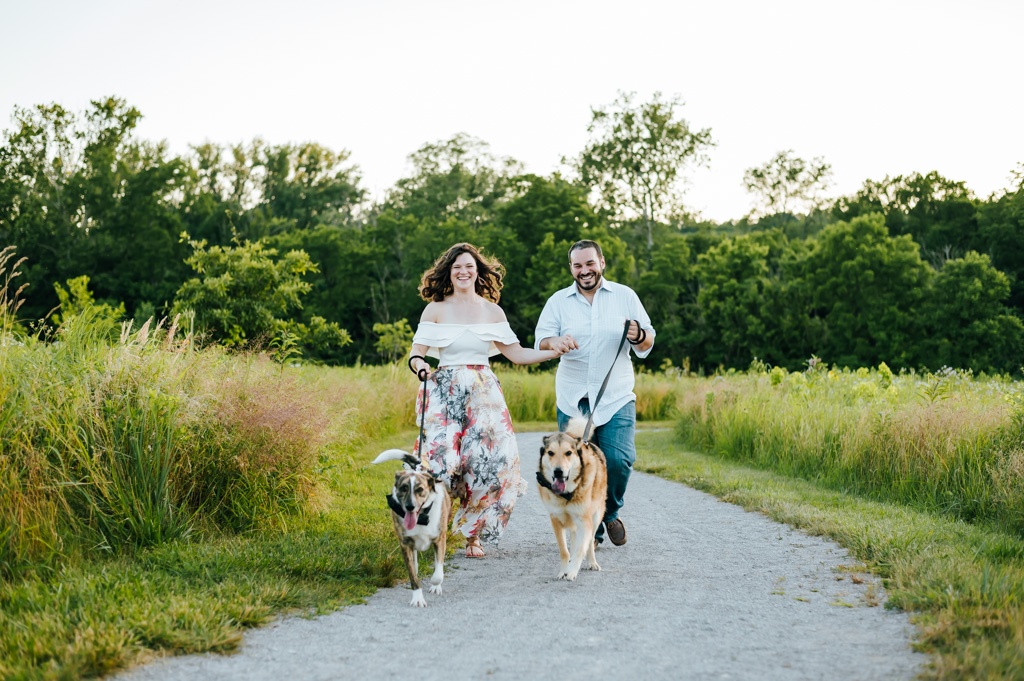 Couple runs with their dogs through a field of grass
