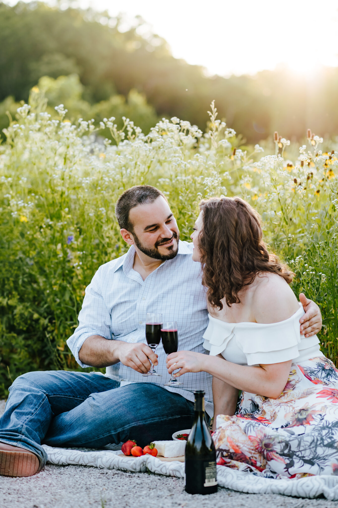 A couple shares a glass of wine at a wildflower picnic engagement session