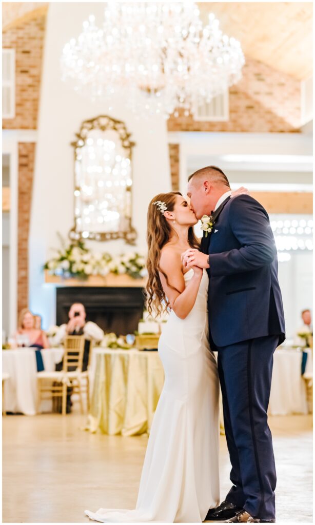 A couple kisses during their first dance under a bright chandelier