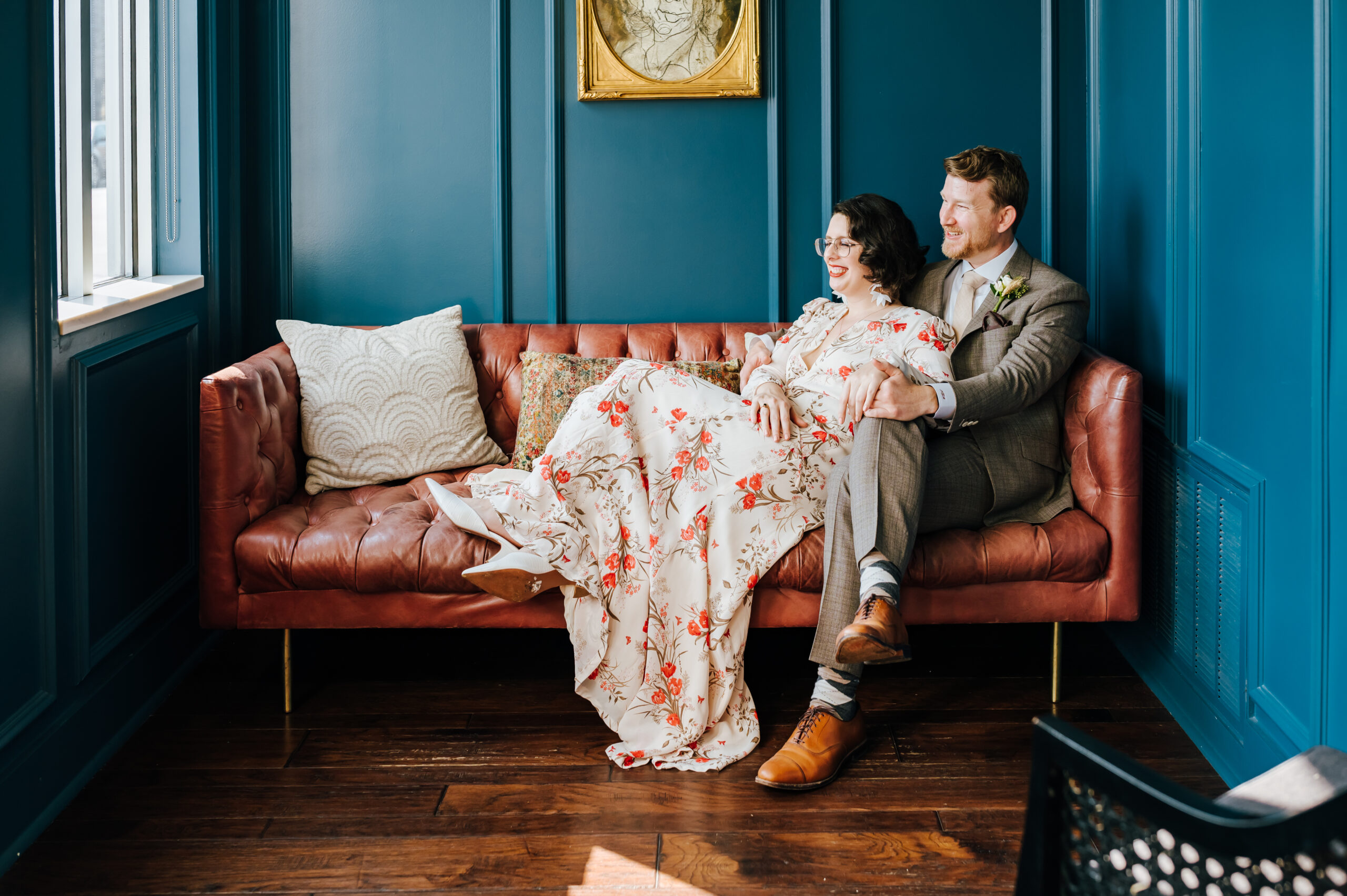 Newlyweds look out the window as they sit on a pink leather couch