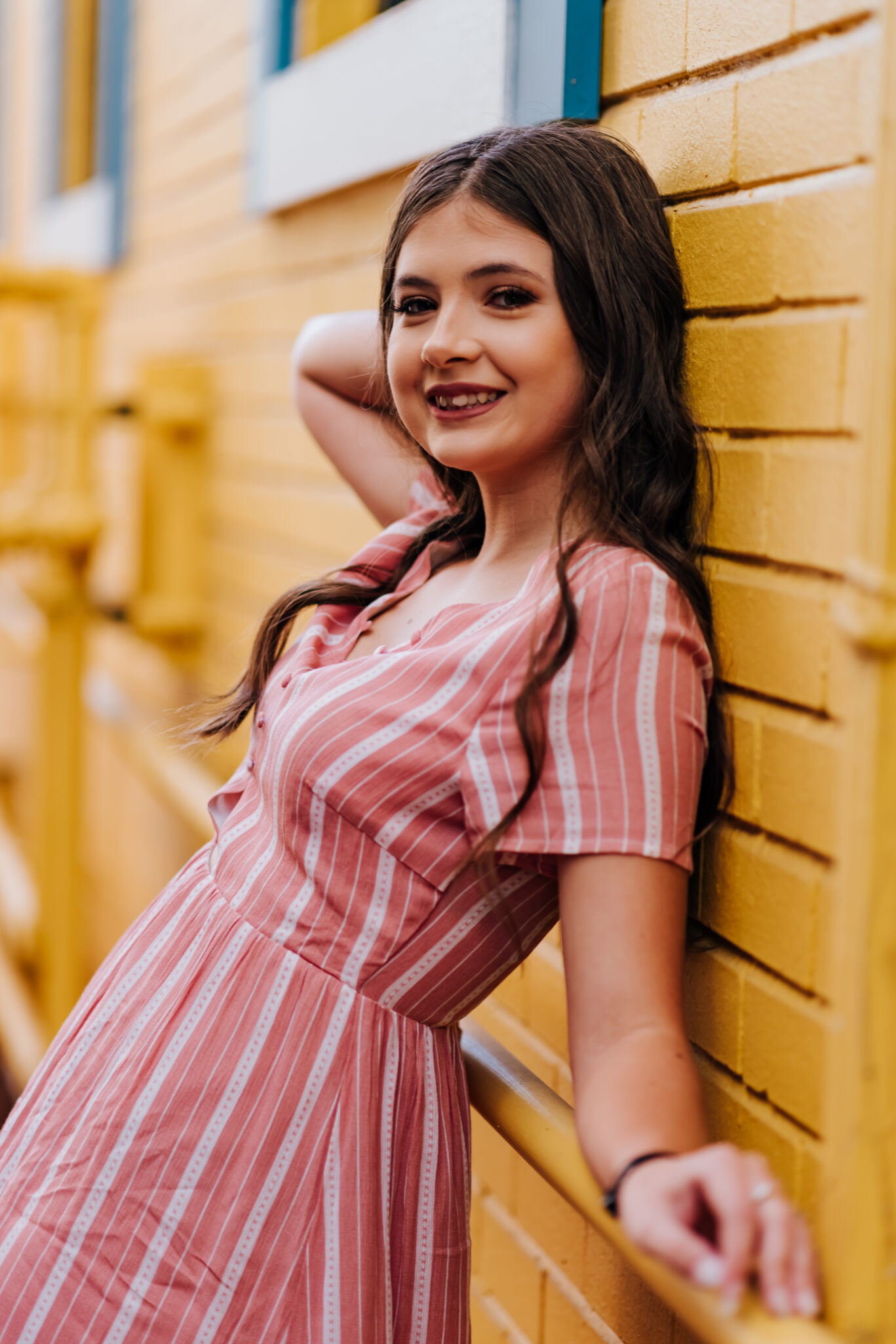 A girl in a pink dress poses against a bright yellow wall