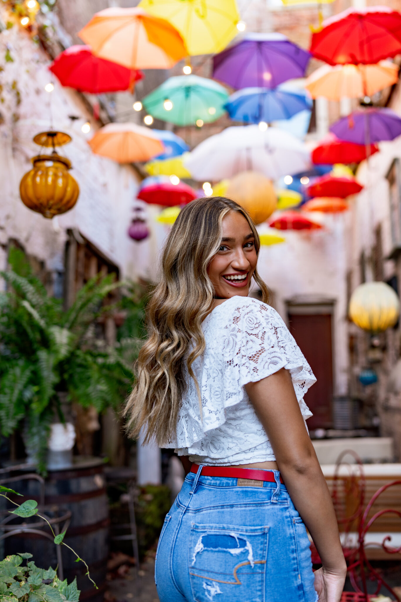 A girl wearing a white top and blue jeans looks over her shoulder with colorful umbrellas above her