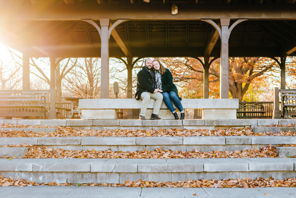 An engaged couple sits on a stone park bench enjoying their engagement