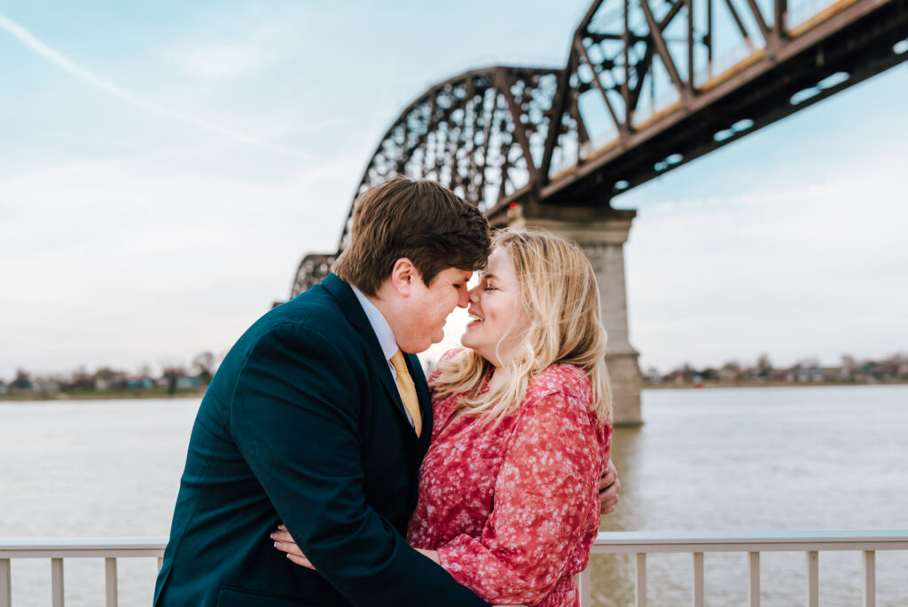 A couple sweetly embraces in front of the beautiful Ohio River and the Big Four Bridge