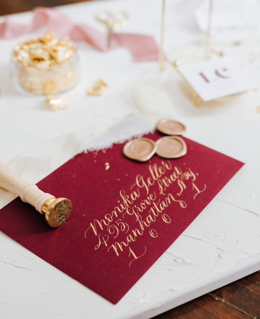 A finished burgundy envelope with gold script surrounded by wax seals and a stamp