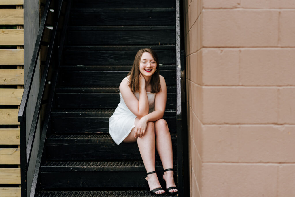 A girl in a white dress sits on a black staircase outdoors