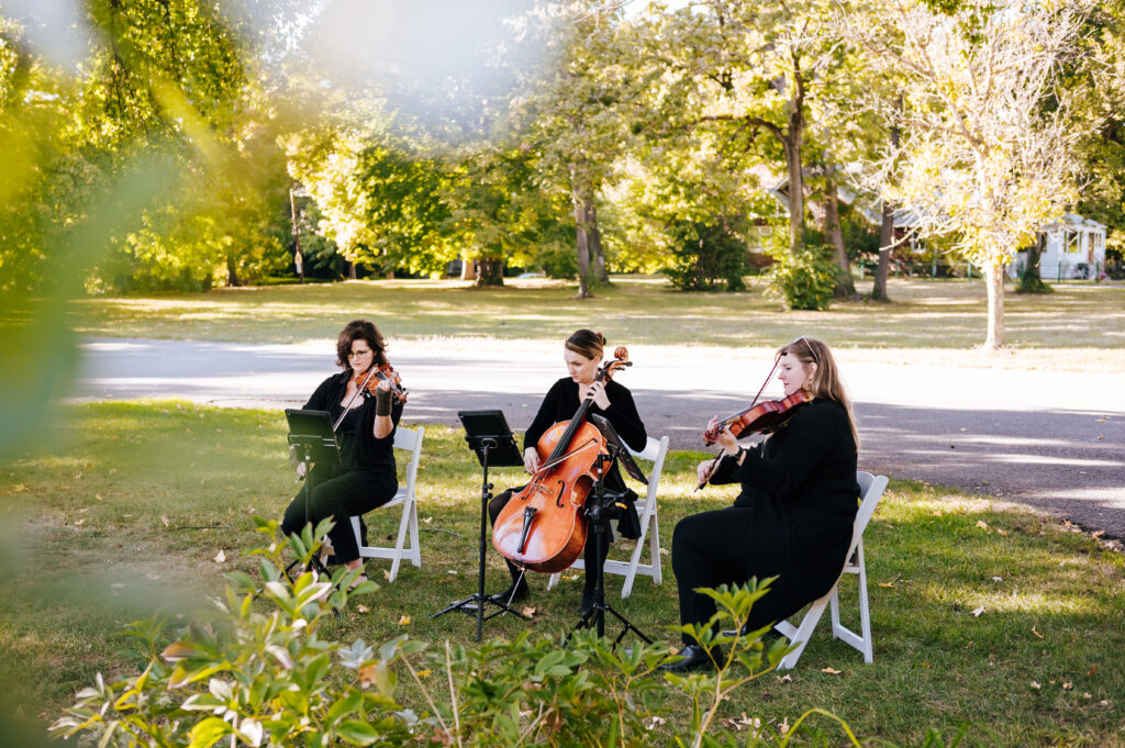 A string trio named Electria plays in a grassy garden before a wedding