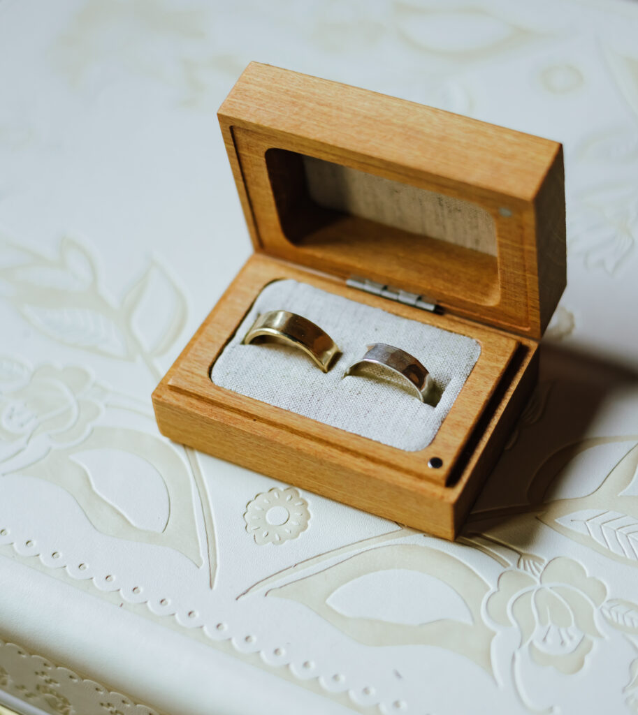 A handcrafted wooden ring box holds two gold wedding bands