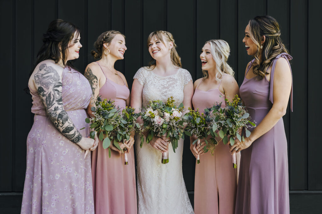 A bride and her bridesmaids, dressed in pink and purple, hold their colorful bouquets