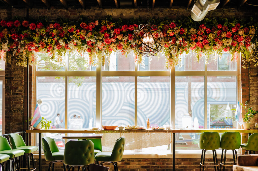 The window display at Trouble Bars, featuring retro green barstools and a floral display overhead