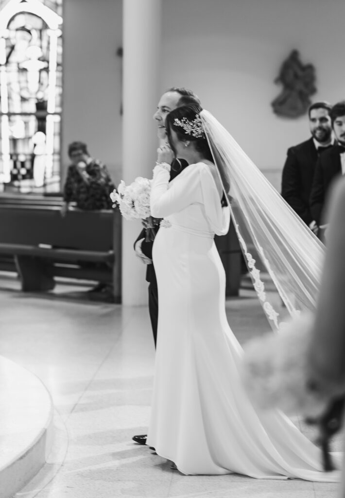 A black and white photo of the bride wiping away happy tears at the altar