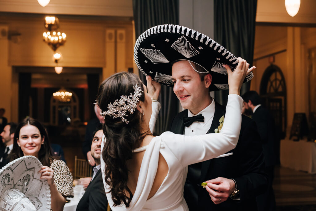 The bride places a mariachi hat on her groom