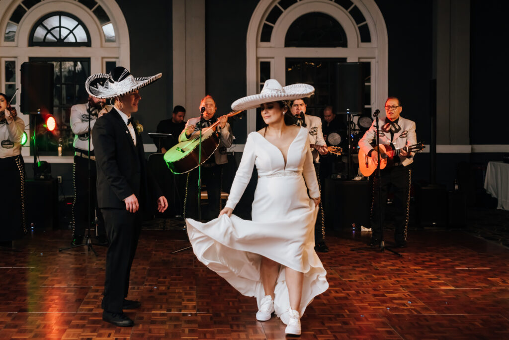 The Mexican bride and her groom dance with Mariachi hats on while the band plays and sings in the background