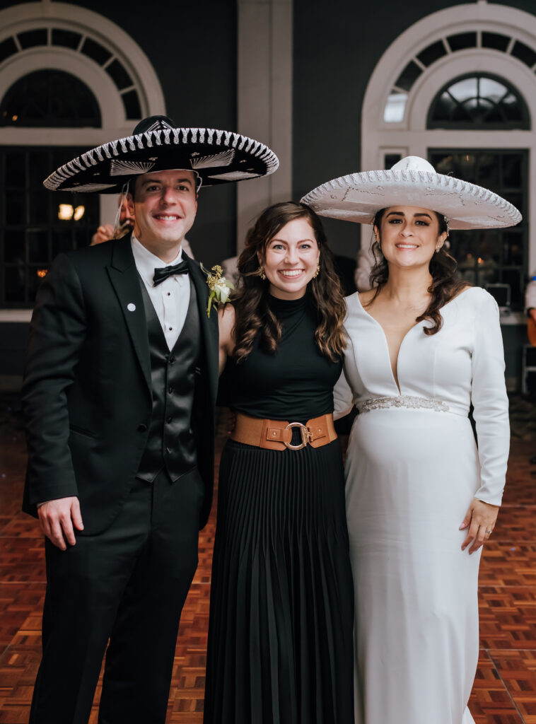 Johanna (photographer here) stands with the newlyweds for a photo as they wear their mariachi hats