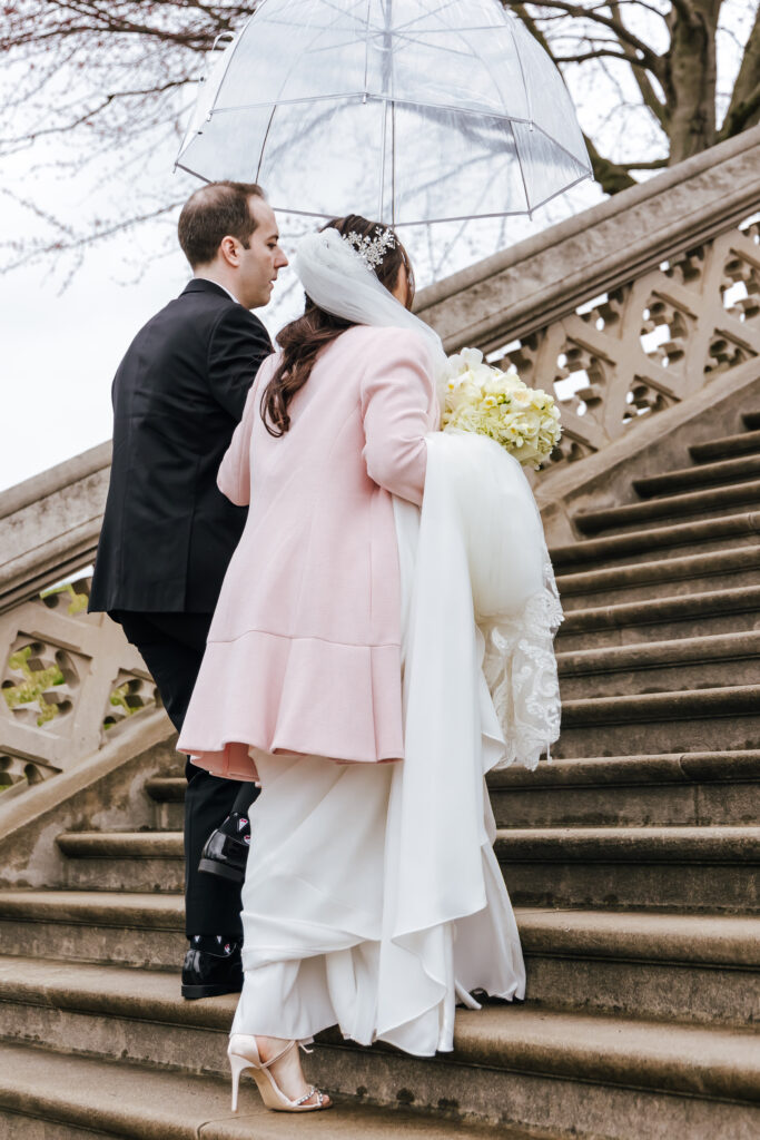 The bride and groom walk up the stairs with an umbrella to stay dry
