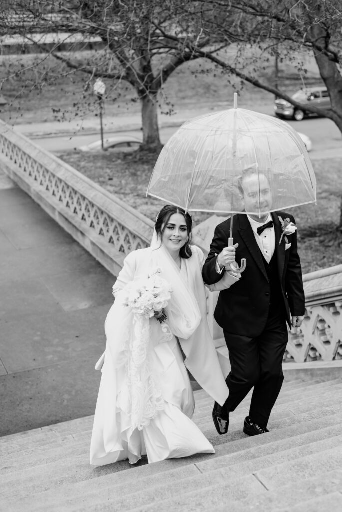 A black and white portrait of the couple walking upstairs with their umbrella to stay dry
