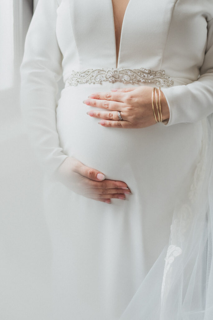 The beautiful bride poses with one hand above and one hand below her baby bump