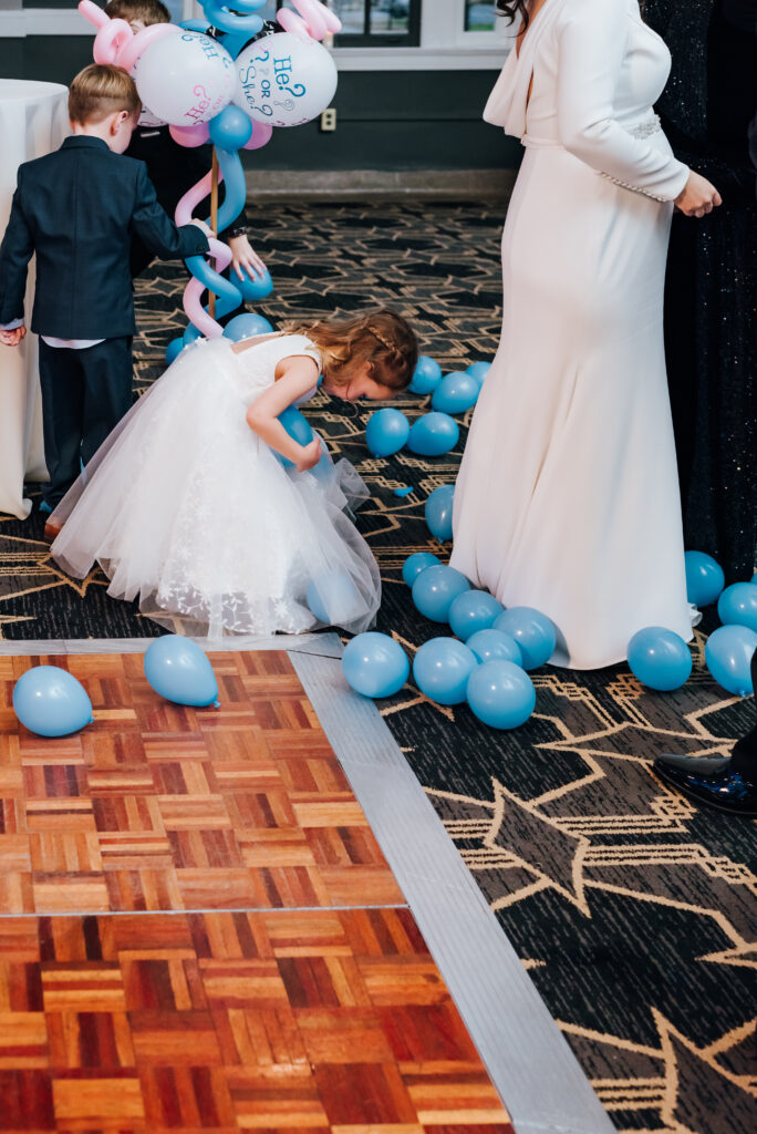 A little flower girl rushes to collect the blue balloons to play with