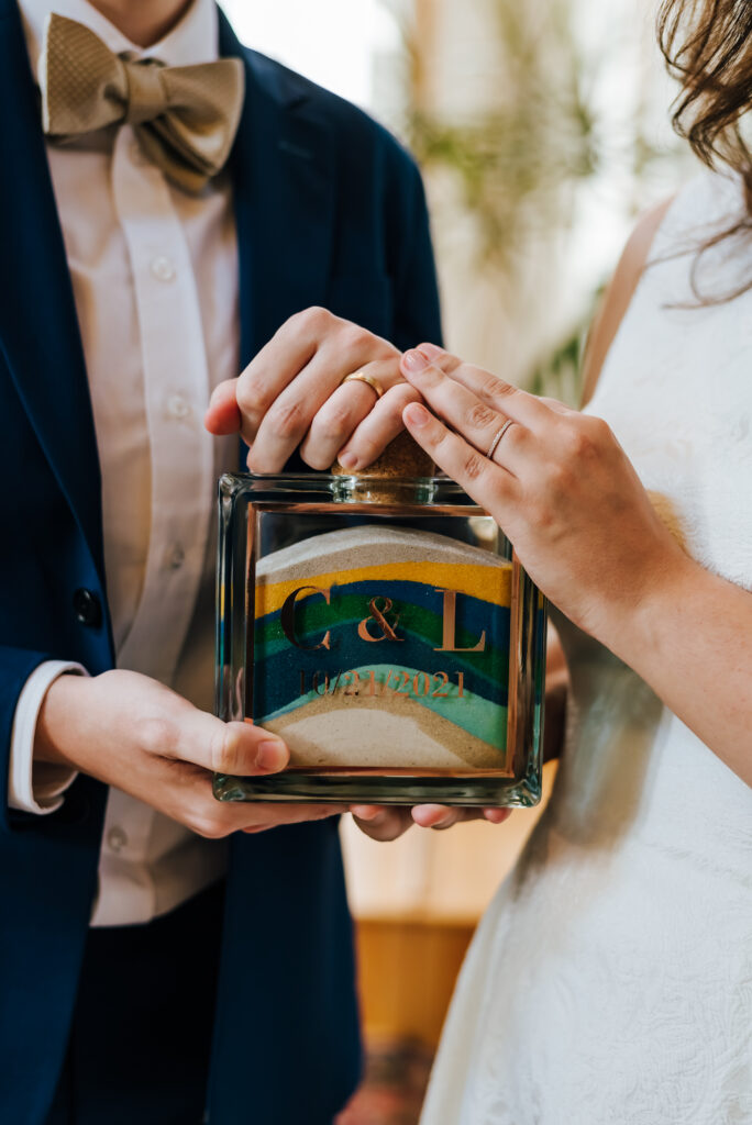 Calley and Lillian hold the glass jar engraved with their initials, now filled with sand in shades of blue, turquoise, gold and white