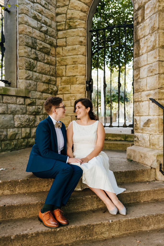 The newlyweds sit on the outer church steps and smile at each other