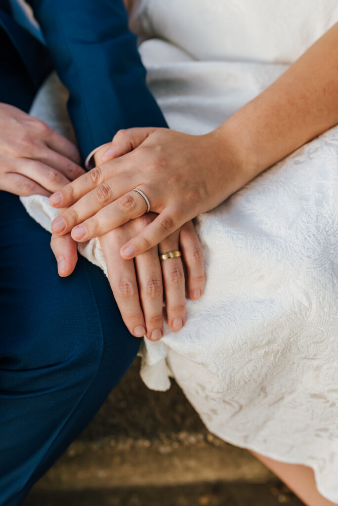 A top down image of the bride's hands with their wedding rings set gently on their laps