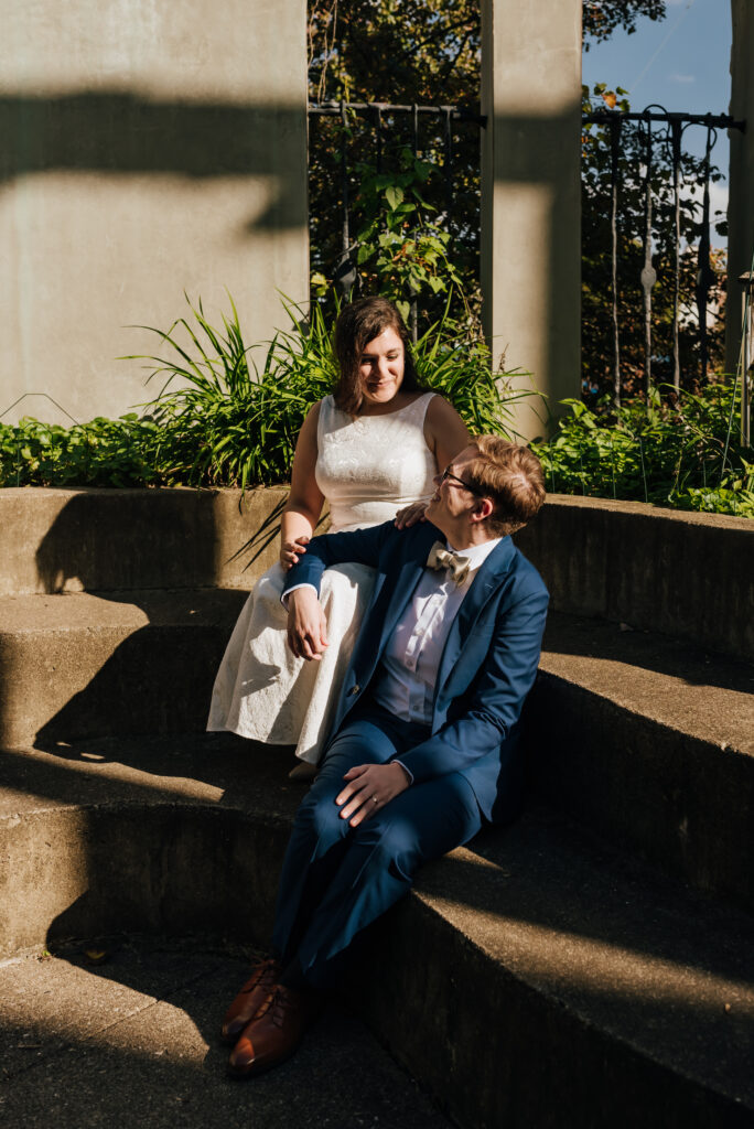 The newlyweds sit on the patio steps outside the church for a harsh light photo with some dramatic shadows