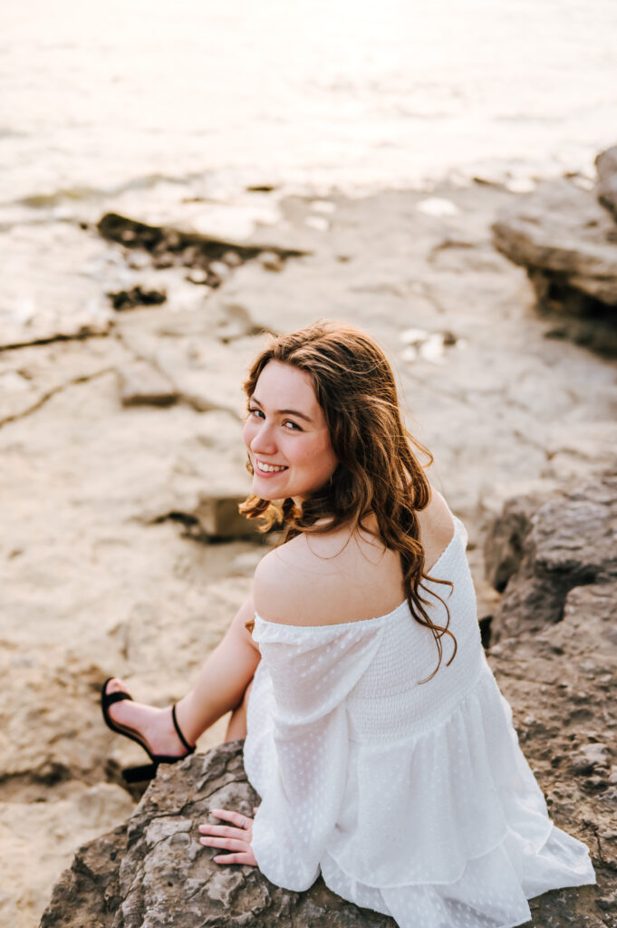 A closeup of a happy high school senior smiling as she sits on a rock over the water