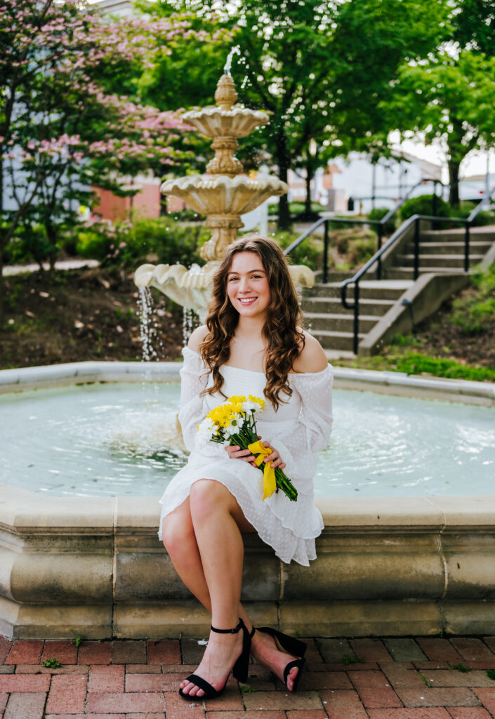 A close up of a high school senior seated by a beautiful fountain