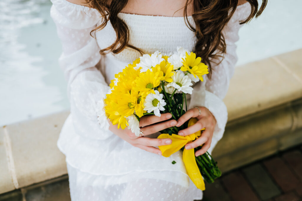 A girl in a white dress holds a bouquet of yellow and white daisies in honor of her deceased grandmother