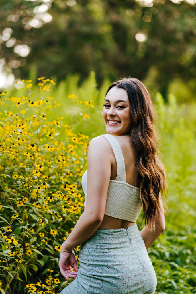 A smiling high school senior girl poses in a field of yellow wildflowers