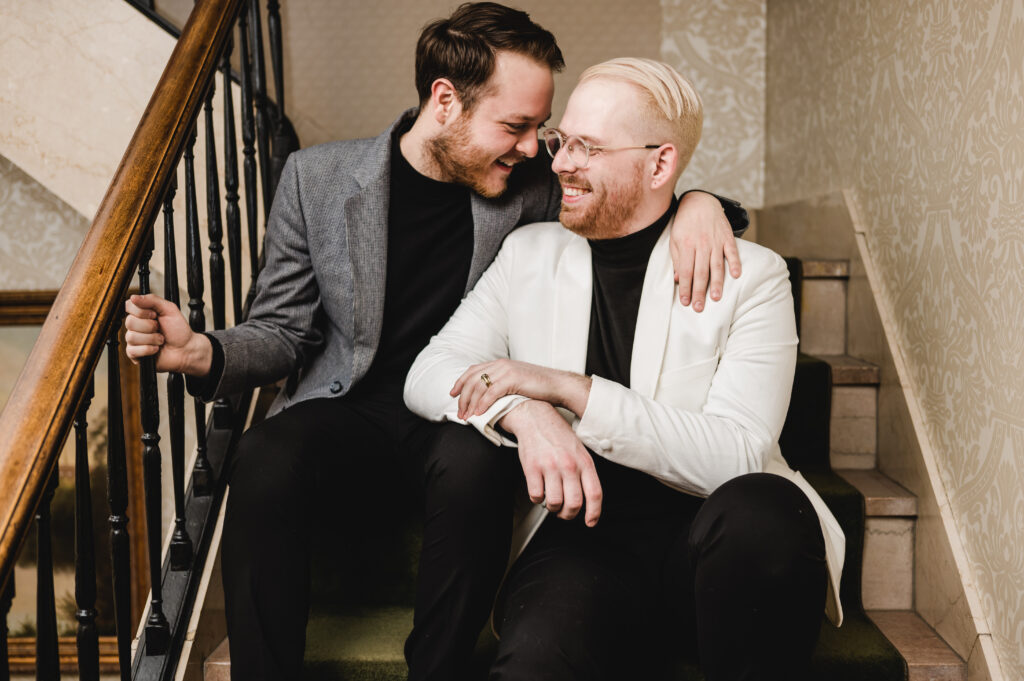 Two engaged men sit on a hotel staircase and look lovingly into each other's eyes