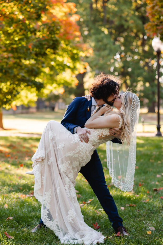 A groom dips his bride for a dramatic kiss in a park of colorful maple trees
