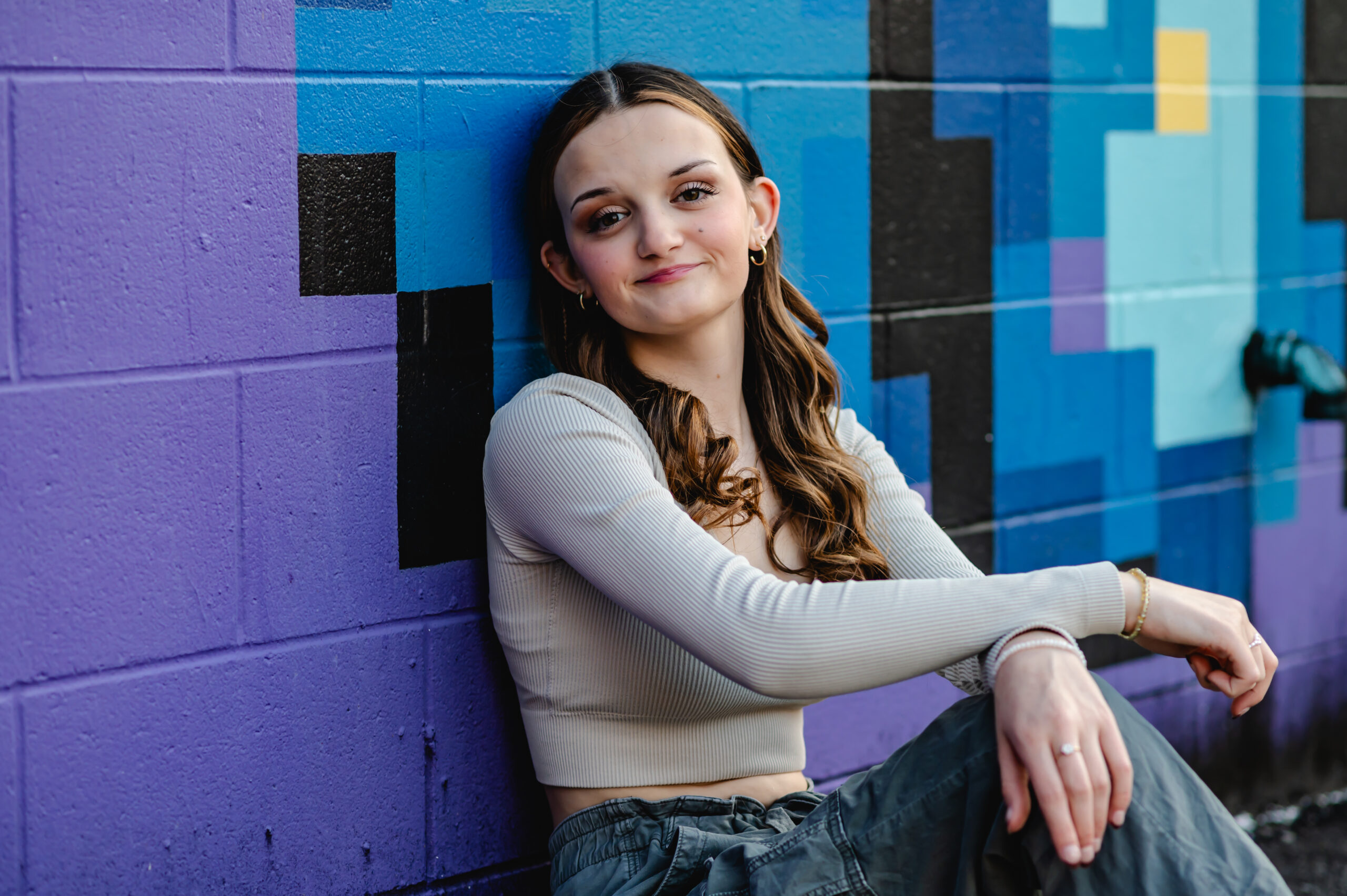 A senior portrait of a girl sitting in front of a colorful purple and blue wall