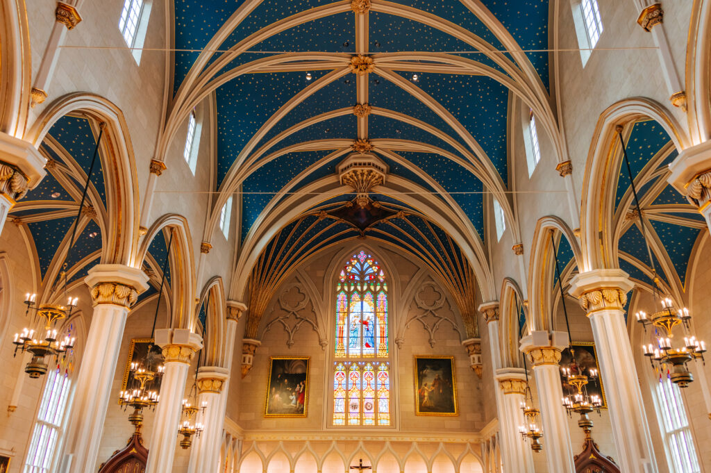 A wide angle photograph shows the magnitude of the vaulted blue and gold ceilings and arched pillars of the interior of the Cathedral of the Assumption 