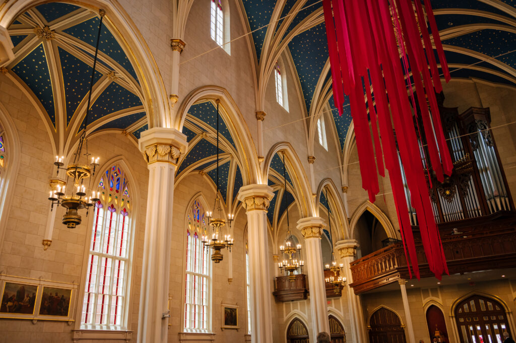 An interior view of the Cathedral of the Assumption shows its tall, vaulted ceilings, red streamers hanging from them, and arched pillars on the sides