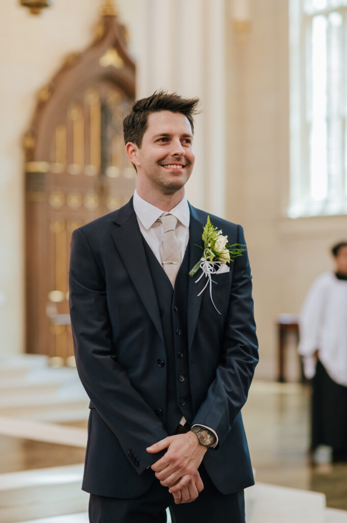 The groom smiles as he waits for his bride at the altar