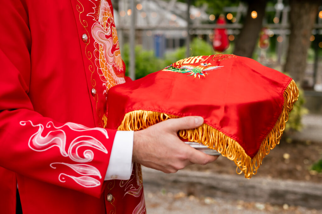 The groom holds a tray covered with a red silk scarf and gold fringes