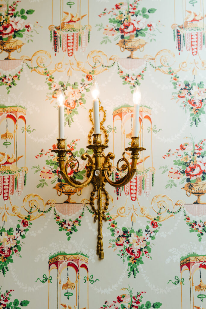 A photo of a golden candle sconce with a vintage patterned wallpaper