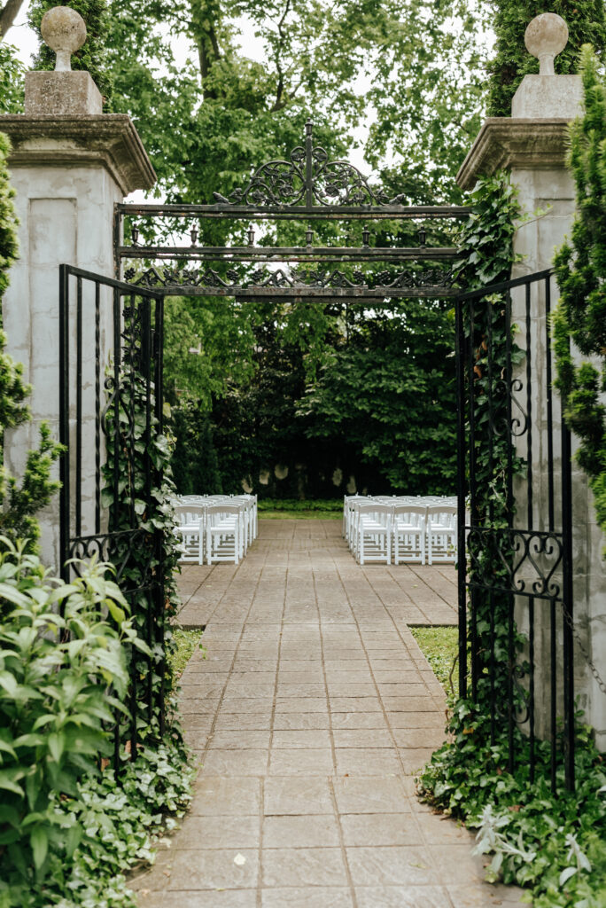An ivy covered gate leads into a garden wedding ceremony setup