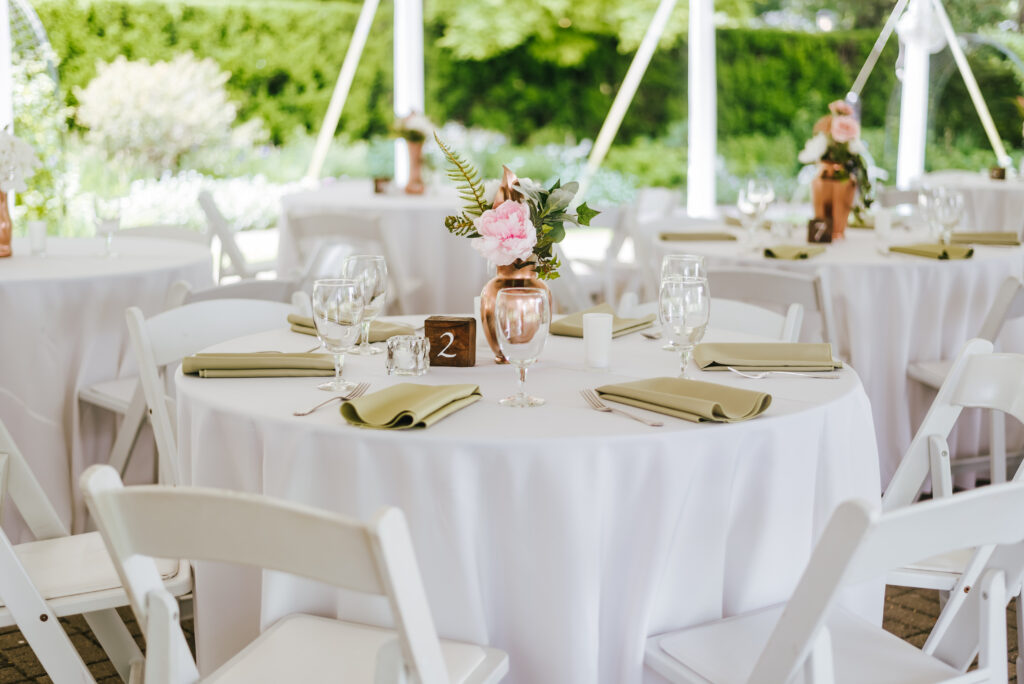 A reception table decorated with white tablecloths, green napkins and copper accents