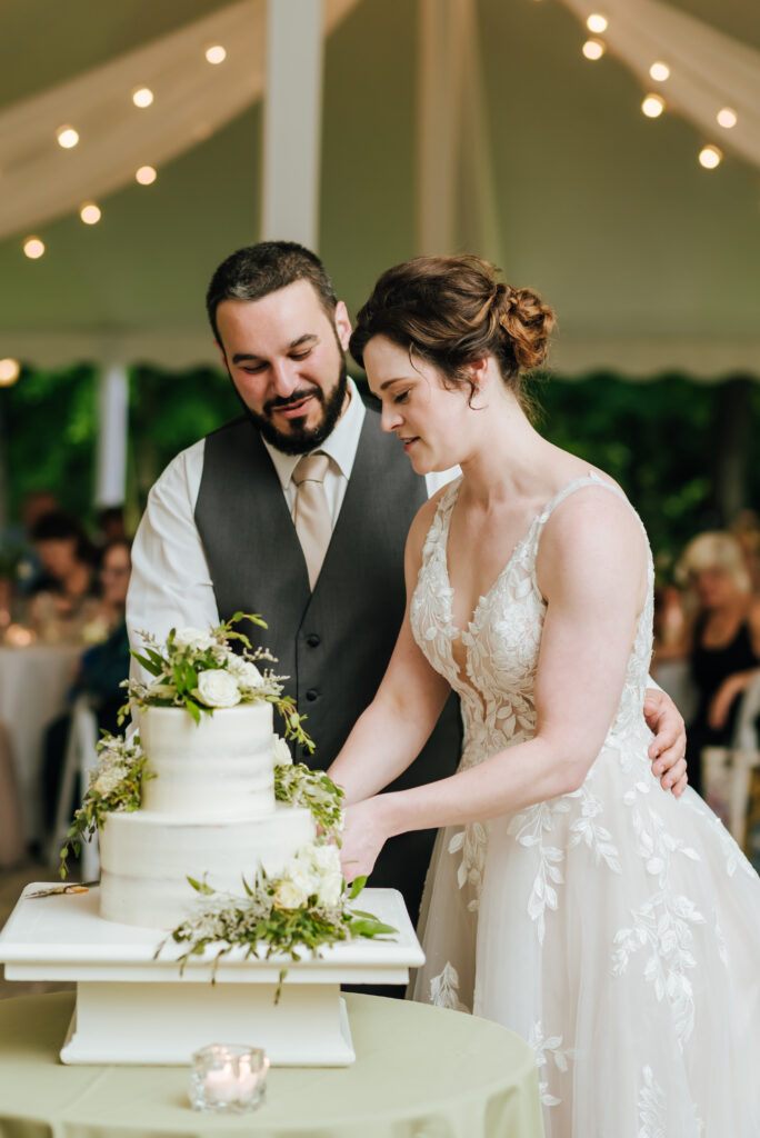 The couple cuts into their white wedding cake with green fern accents