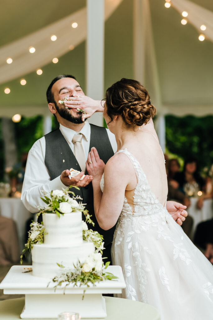 A mischievous bride generously shoves cake onto her groom's face