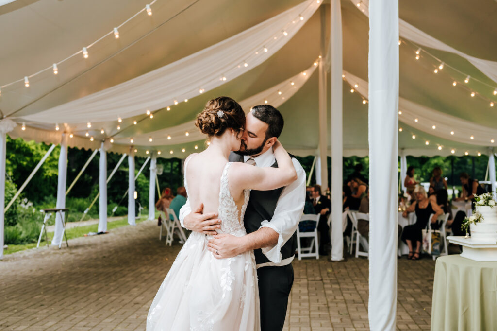 A couple shares their first dance as newlyweds under string lights and a canopy tent